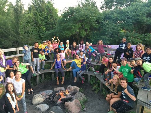 Group of campers and counselors smiling around fire pit